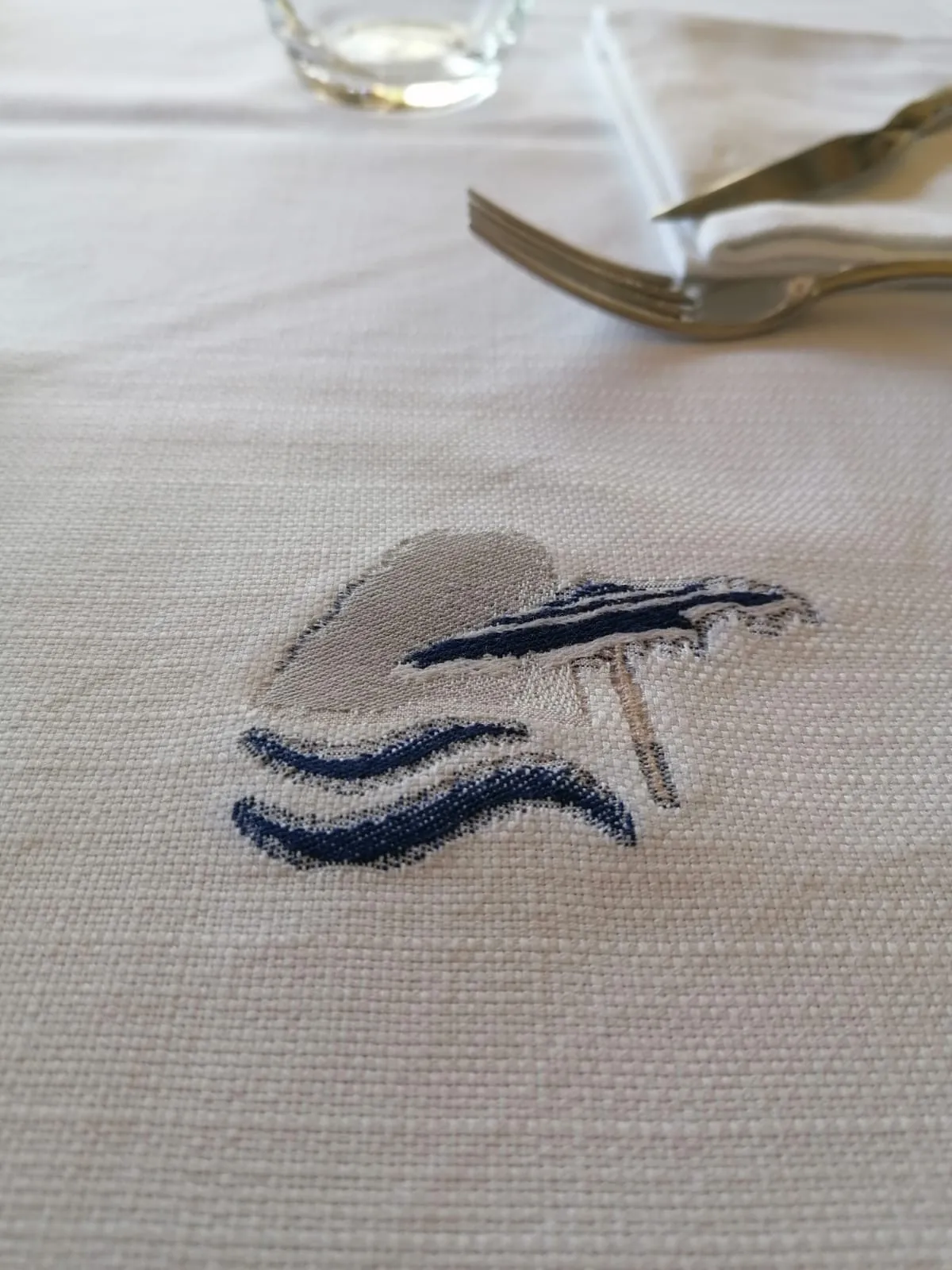 Dettaglio del ricamo dell'emblema Fontelina Beach Club — ombrellone e onde su tovagliato Capuano