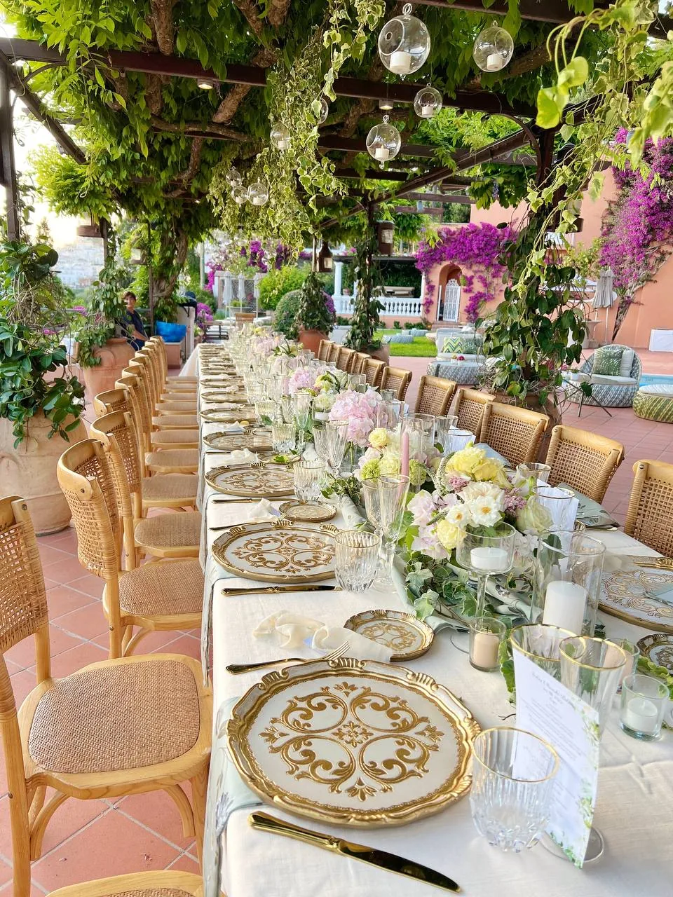 Banchetto wedding sotto pergolato di glicine con piatti dorati e fiori